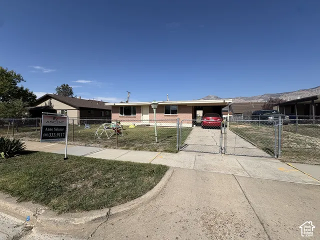 Single-story brick exterior, attached carport, fenced front yard, concrete driveway, and mountain backdrop