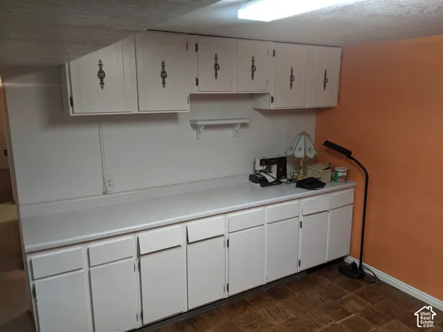 White cabinetry, white countertops, built-in shelving, overhead lighting, wood-finish flooring