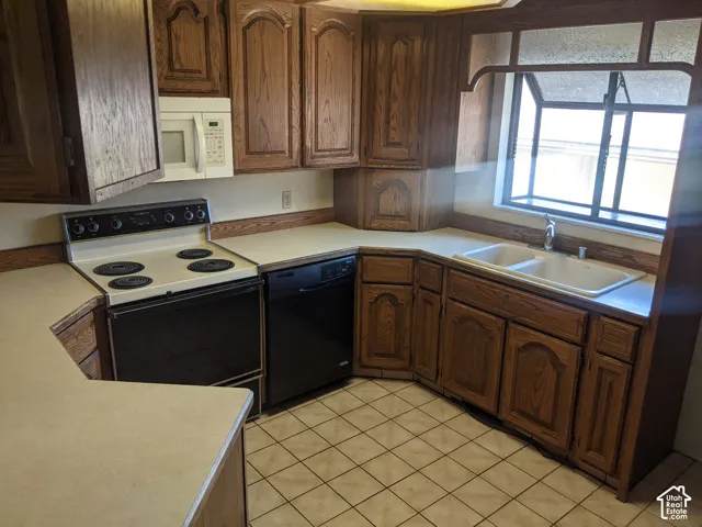 Kitchen featuring wood cabinetry, light-toned countertops, a built-in double sink, and tiled flooring