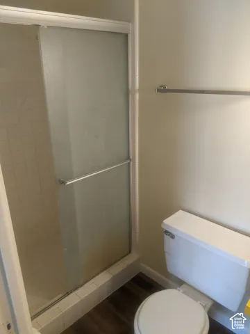 Shower enclosure with frosted glass sliding doors, white tile surround, and wood-finish flooring
