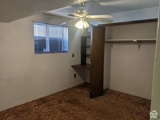 Spacious bedroom featuring carpeted flooring, a ceiling fan with integrated lighting, and an expansive walk-in closet with built-in shelving and rod system