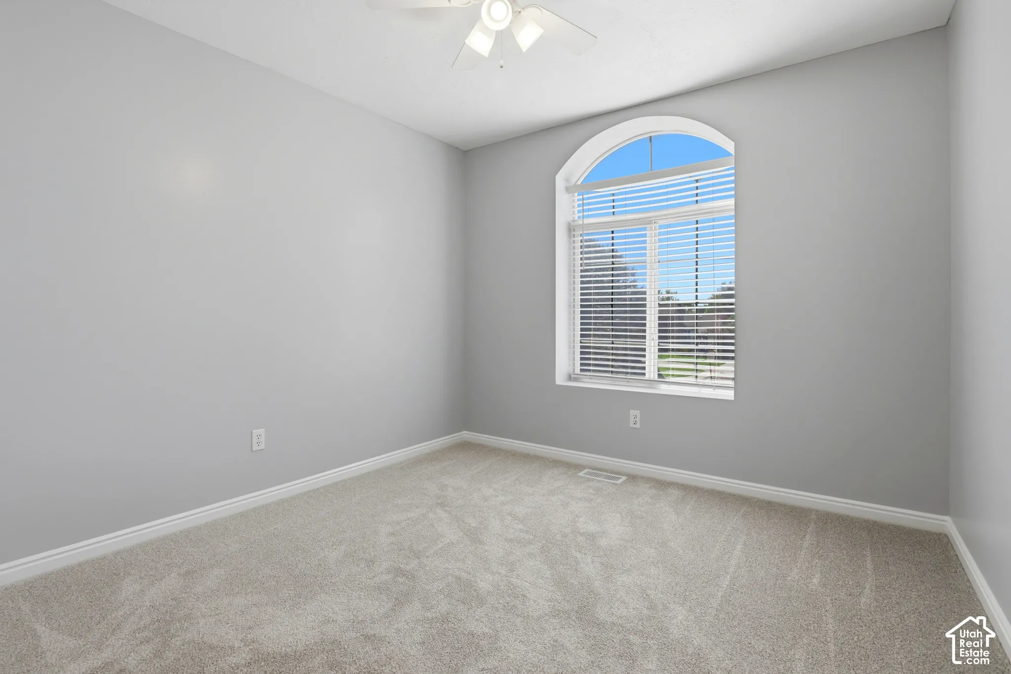 Arched window with blinds, light-toned carpeting, and a ceiling fan