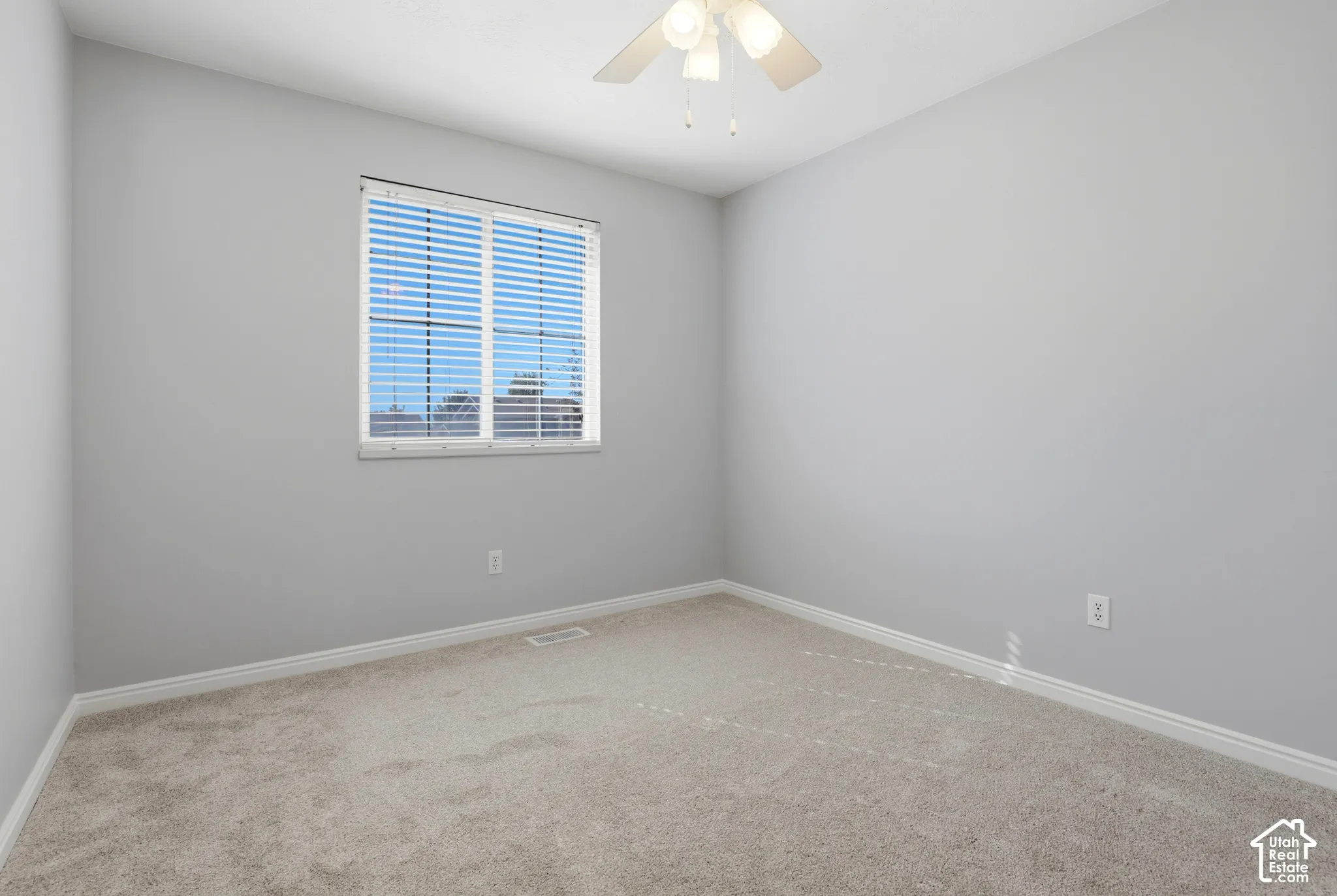 Neutral-toned carpeted flooring, a window with horizontal blinds, light gray wall finishes, a white ceiling fan, and white trim