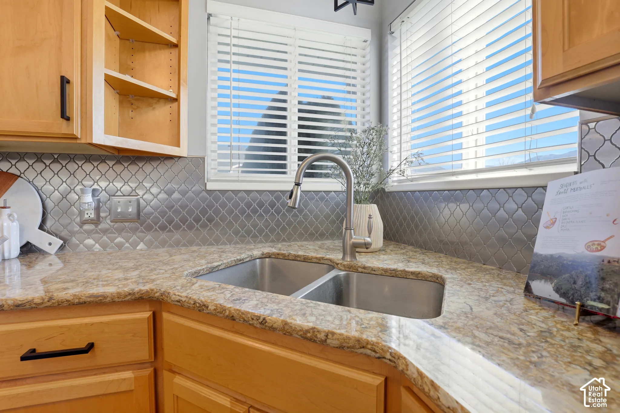 Dual basin stainless steel sink with a high-arc faucet, granite-finish countertops, honeycomb-patterned backsplash, and natural wood cabinetry