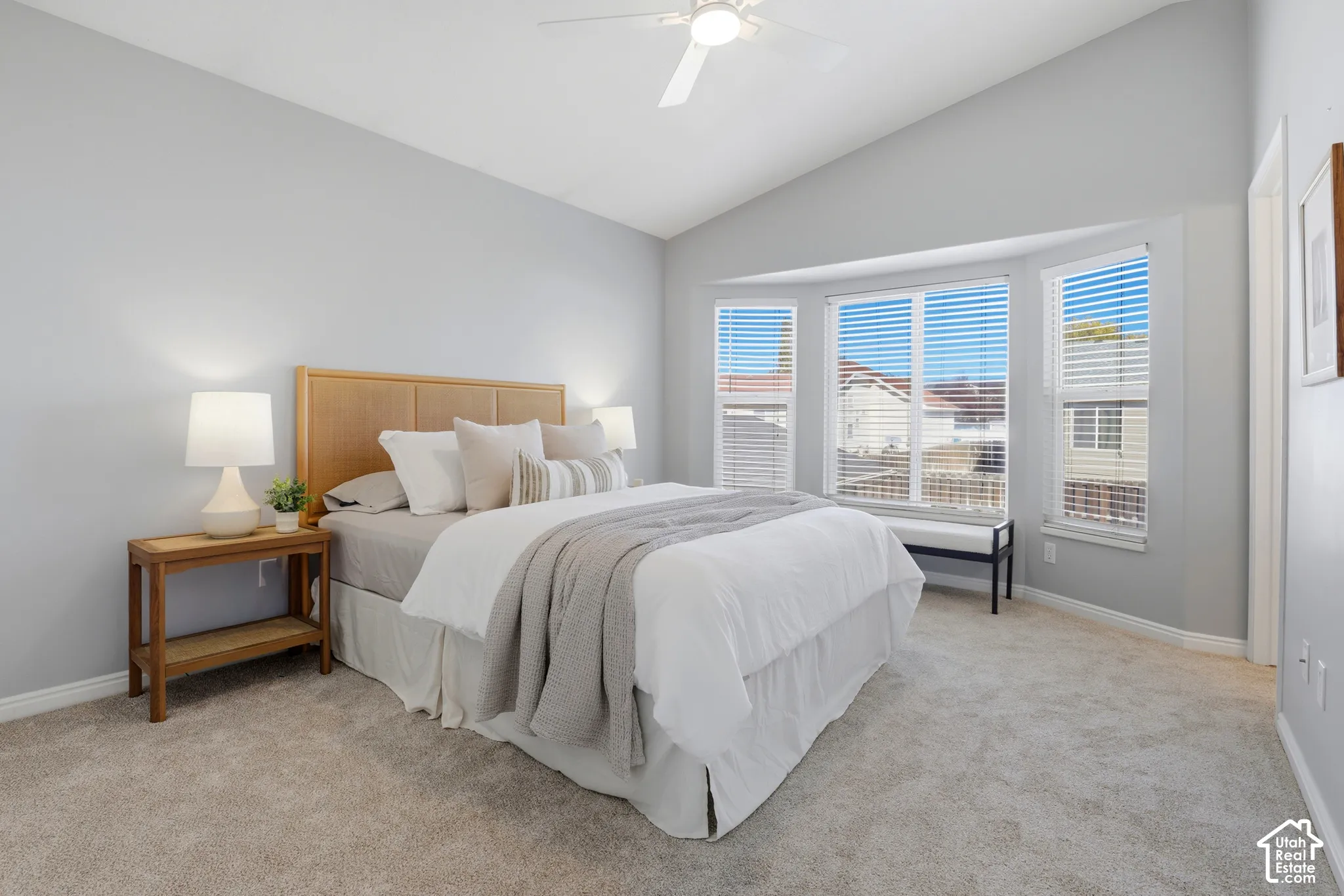 Vaulted ceiling with a ceiling fan, bay window with blinds, and neutral carpeting