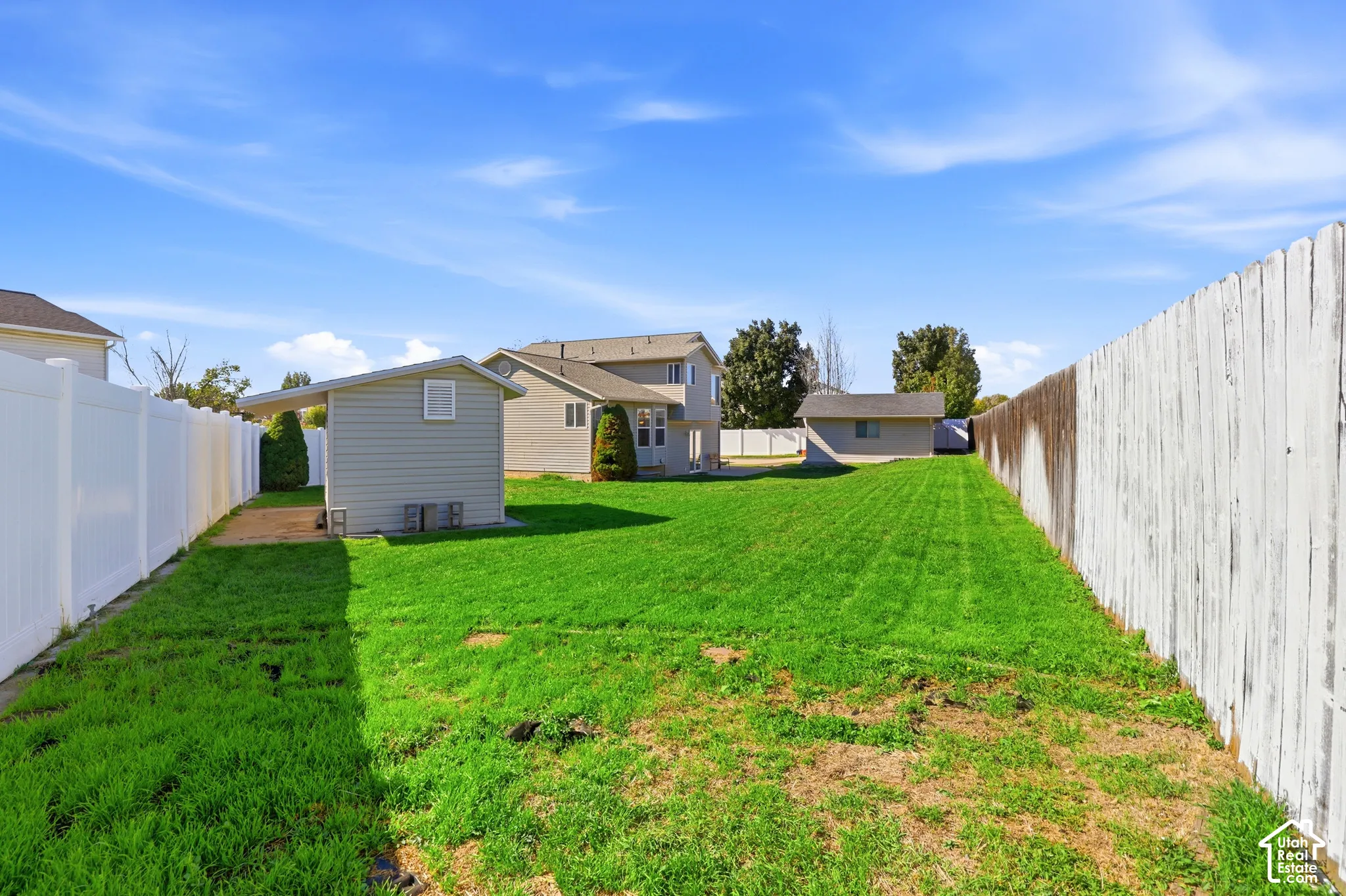 Expansive backyard featuring a manicured lawn, white privacy fencing, and two sheds with exterior siding