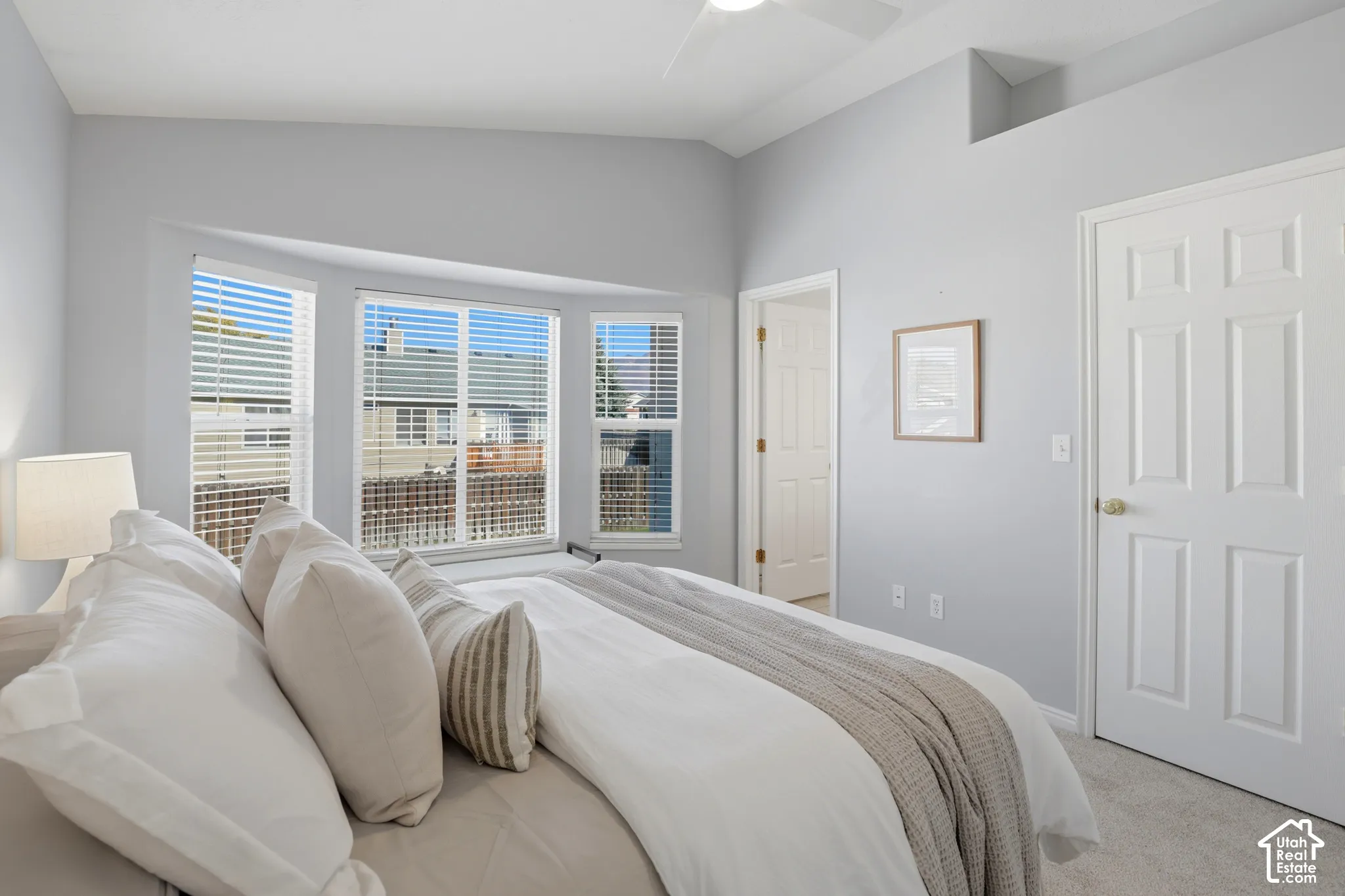 Bay window with horizontal blinds, neutral wall paint, vaulted ceiling, and carpeted flooring