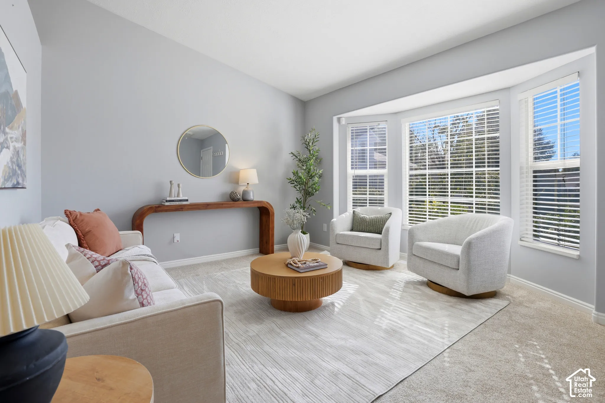 Vaulted ceiling, bay windows with blinds, light gray wall color, light-toned carpet flooring, and a console table