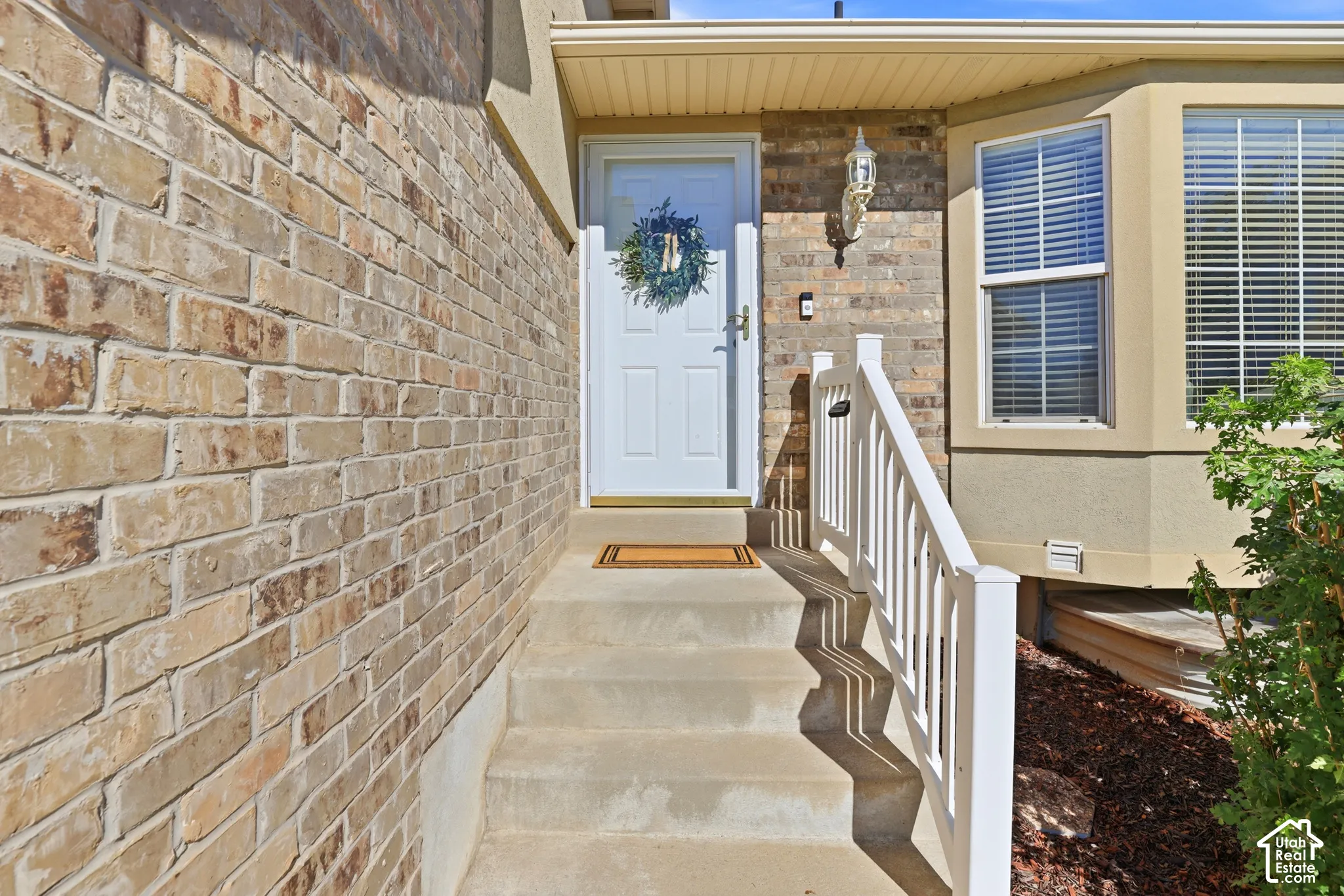 Brick exterior featuring a white entry door, concrete steps, a white railing, and a bay window with blinds