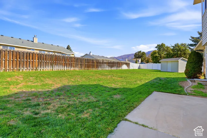 Expansive grassy yard with a concrete patio, wood privacy fencing, and a storage shed