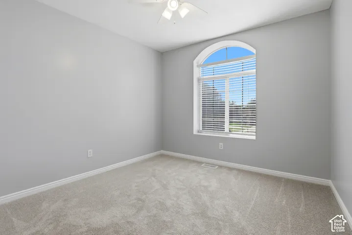 Arched window with blinds, light-toned carpeting, and a ceiling fan