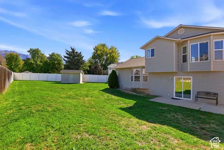 Expansive backyard featuring a manicured lawn, white privacy fencing, and a built-in patio
