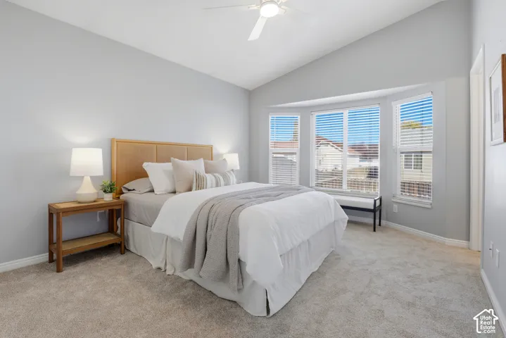 Vaulted ceiling with a ceiling fan, bay window with blinds, and neutral carpeting