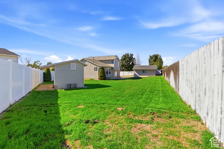 Expansive backyard featuring a manicured lawn, white privacy fencing, and two sheds with exterior siding