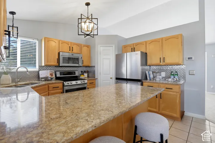 Kitchen featuring a multi-tone countertop peninsula, stainless steel appliances, light wood cabinetry, and recessed tile flooring