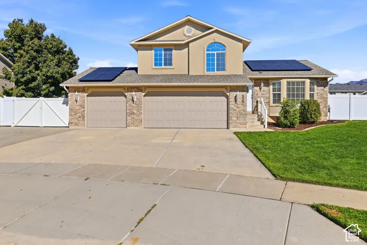 Stucco and stone facade with a two-car garage, solar panels, and a landscaped front yard