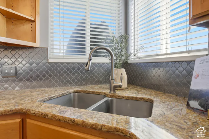 Dual basin stainless steel sink with a high-arc faucet, set within a granite-finish countertop, complemented by a metal arabesque tile backsplash and natural wood-finish cabinetry