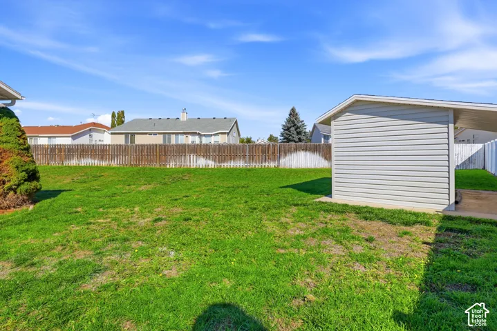 Expansive green space featuring a wood fence, mature landscaping, and a side-gabled carport with horizontal siding