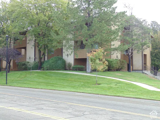 Multi-story building exterior featuring vertical siding, stucco facade, recessed private balconies, and mature landscaping with manicured lawn