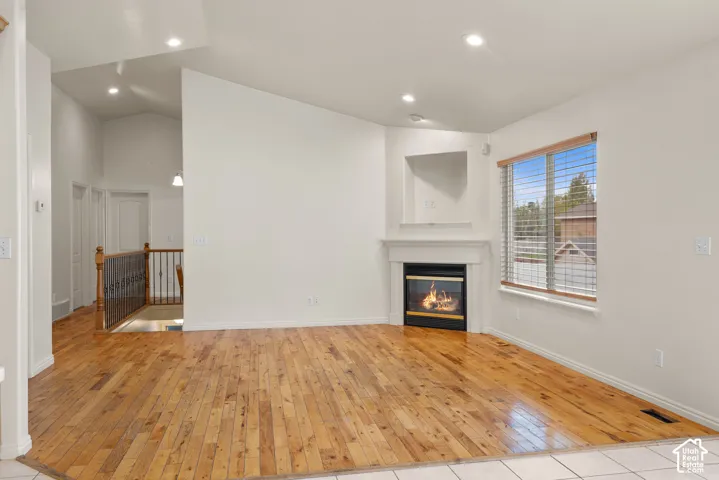 Hardwood flooring, fireplace, recessed lighting, vaulted ceiling, and interior balcony with wood and metal railing