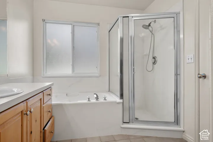 Alcove bathtub with deck-mounted fixtures, separate glass-enclosed shower, wood-finish vanity with countertop and integrated sink, and frosted sliding windows