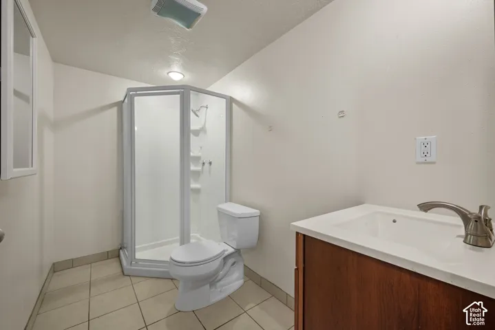 Corner shower enclosure, ceramic tile flooring, single vanity with integrated sink, wood-finish cabinetry, and brushed nickel faucet