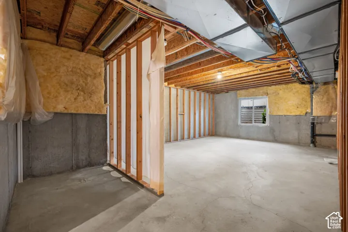 Unfinished basement featuring concrete flooring, exposed wood ceiling joists, framed partition walls, and a window for natural light