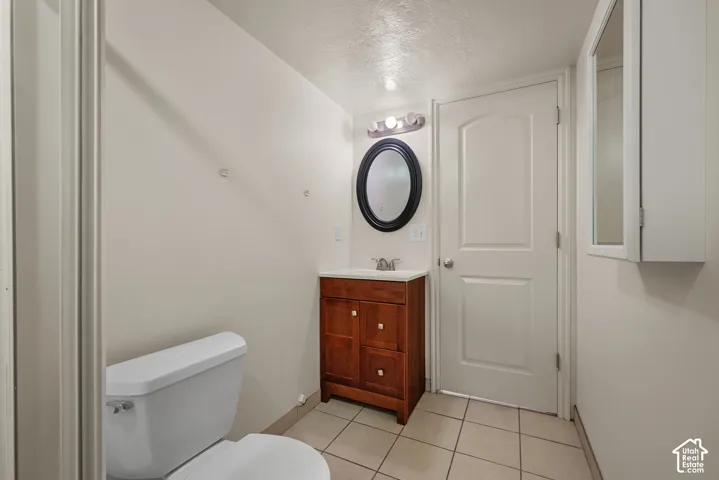 Wood-finish vanity with an oval mirror, tile flooring, and overhead lighting