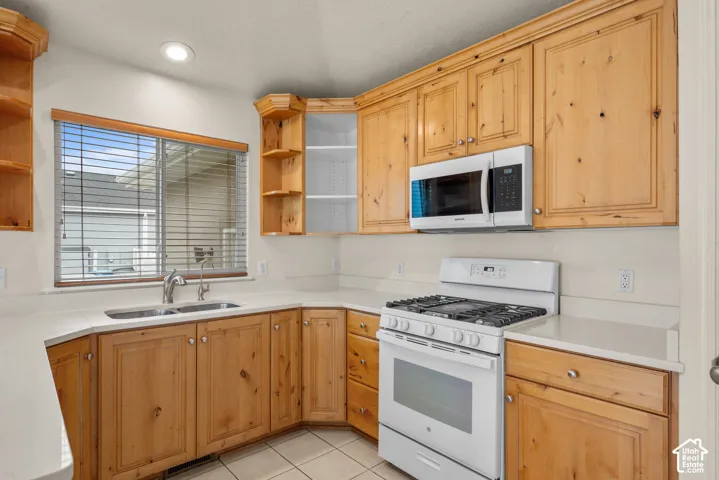 Light wood cabinetry, white countertops, built-in microwave, white gas range, and a double basin sink