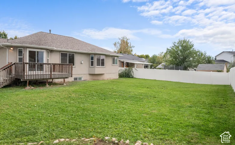 Expansive grassy yard with a white privacy fence, featuring a rear deck with stairs and a bay window