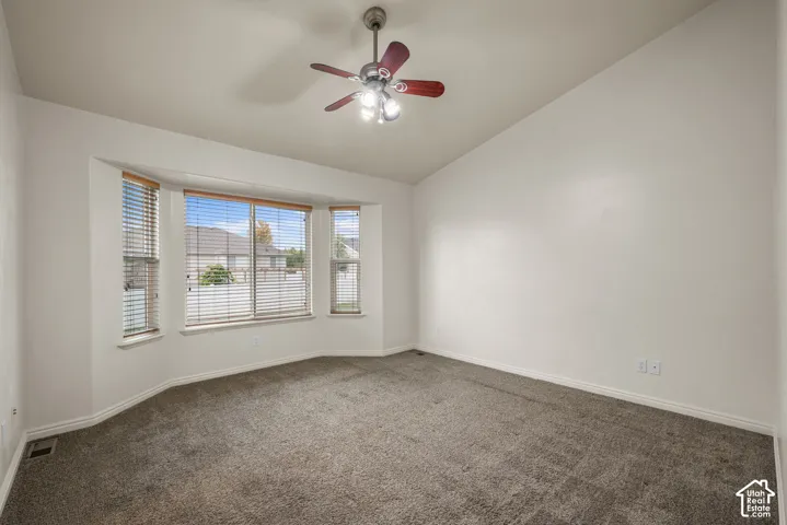 Vaulted ceiling with a ceiling fan, bay window with blinds, and carpeted flooring