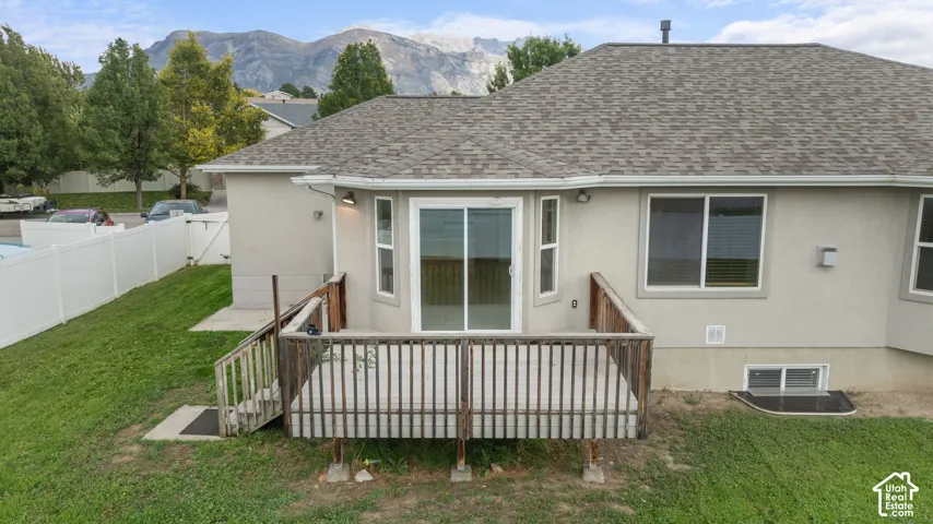 Rear exterior featuring a wood deck with stairs, sliding glass door, multiple windows, and a vinyl privacy fence