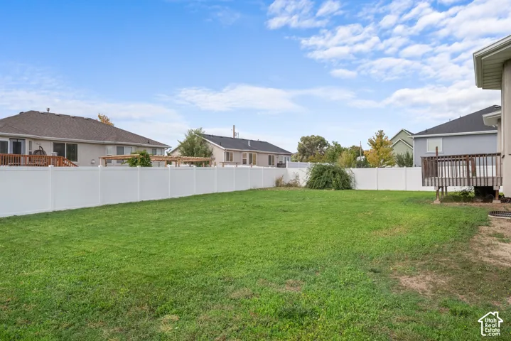 Expansive backyard with a manicured lawn, white privacy fencing, and a wood deck