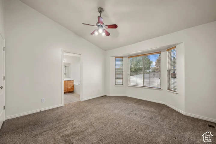 Vaulted ceiling with a ceiling fan, bay window, and neutral carpet