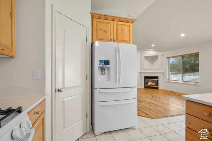 Kitchen area with wood-finish cabinetry, white tile flooring, and a white appliance