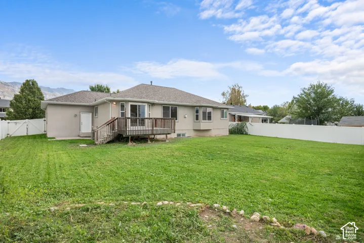 Expansive backyard with a wooden deck, sliding glass doors, and a white privacy fence