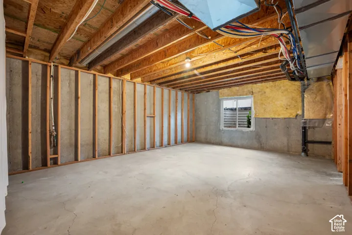 Unfinished basement with concrete flooring, framed perimeter walls, exposed ceiling joists, and a window for natural light