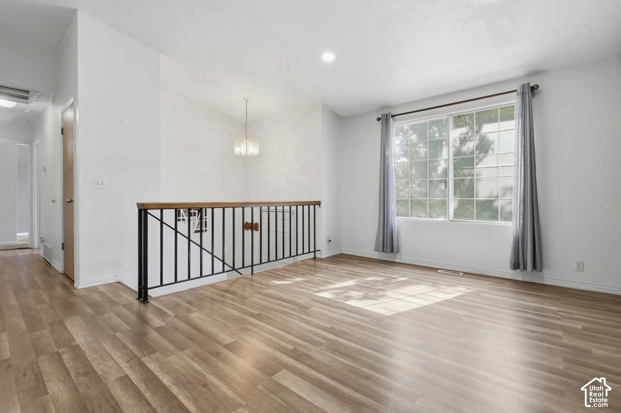 Vaulted ceiling with a contemporary chandelier, wood-finish flooring, and a large multi-pane window