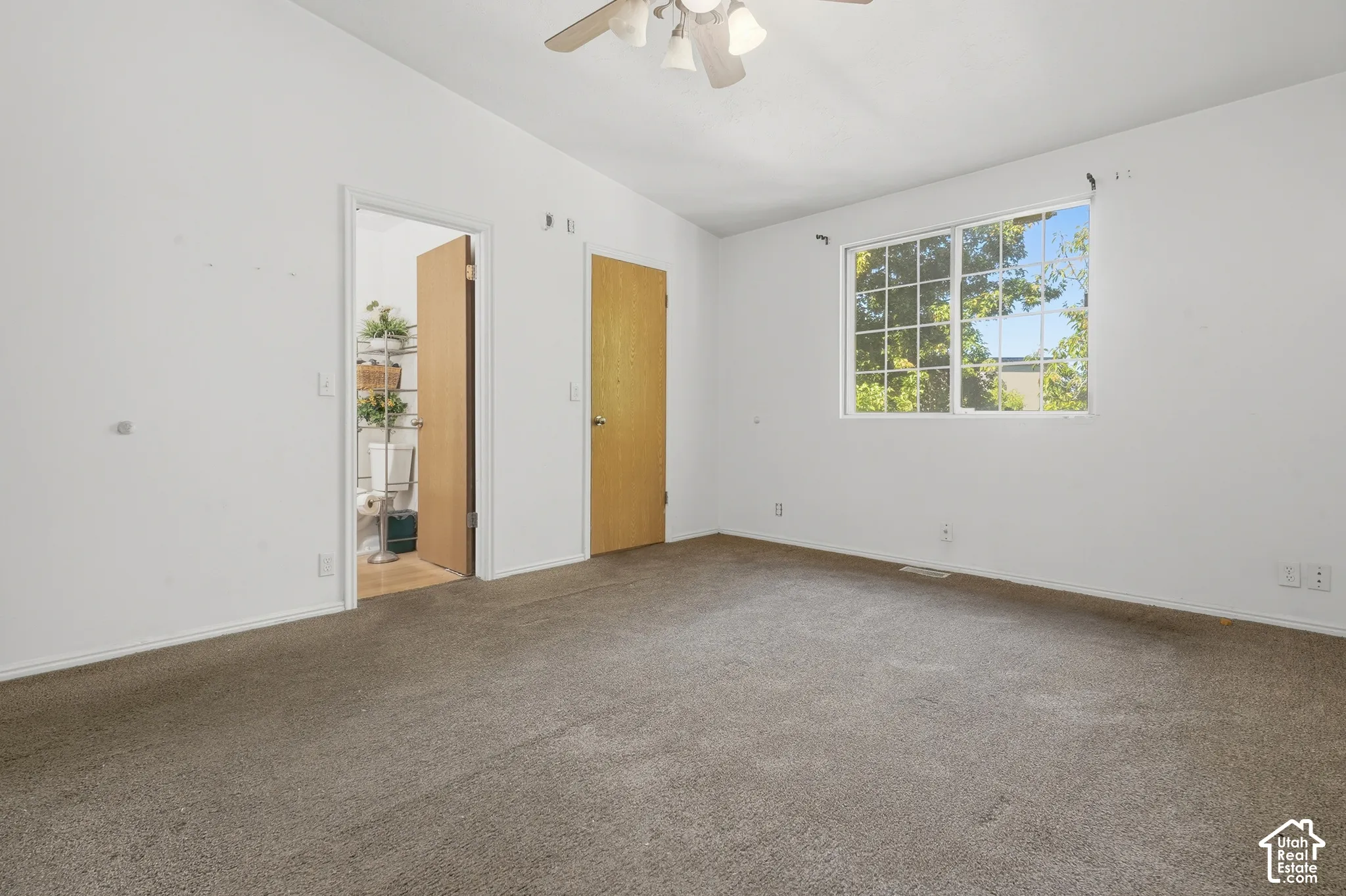 Carpeted flooring, white walls, ceiling fan, window with grid pattern, and wooden doors