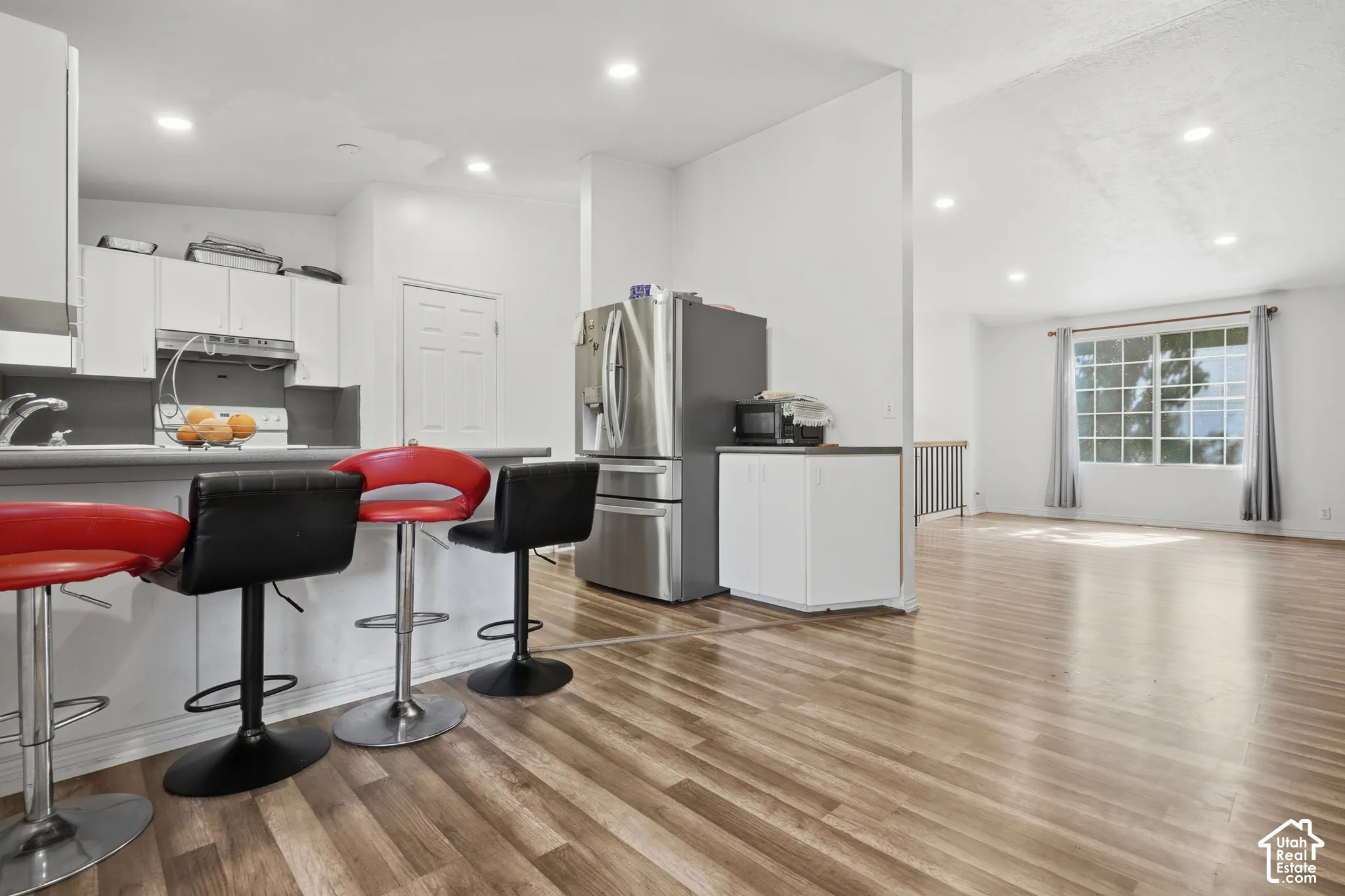 Open concept design with wood-finish flooring, white cabinetry, recessed lighting, and a large window