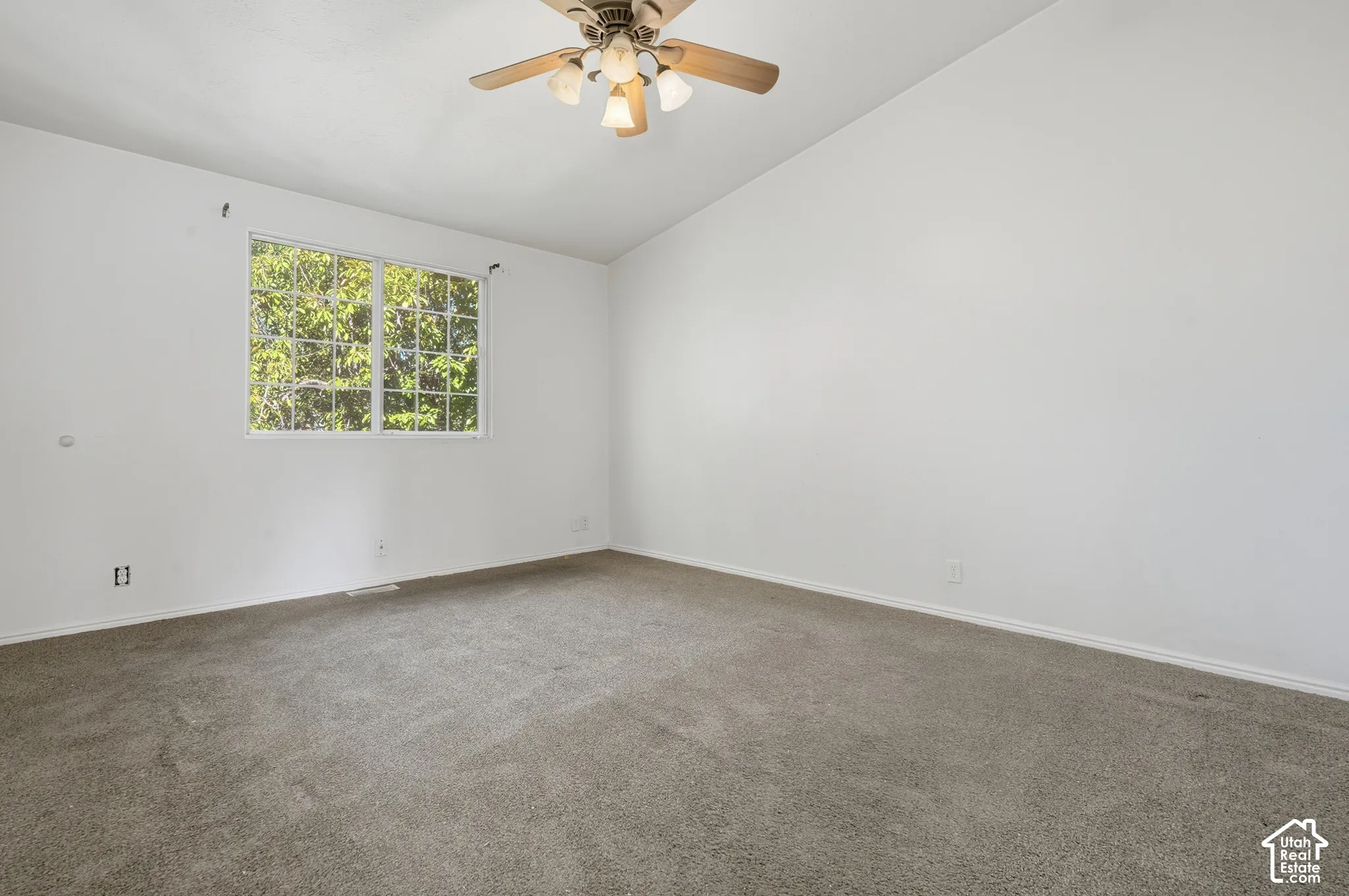 Vaulted ceiling with a ceiling fan, carpeted flooring, and a multiple-pane window