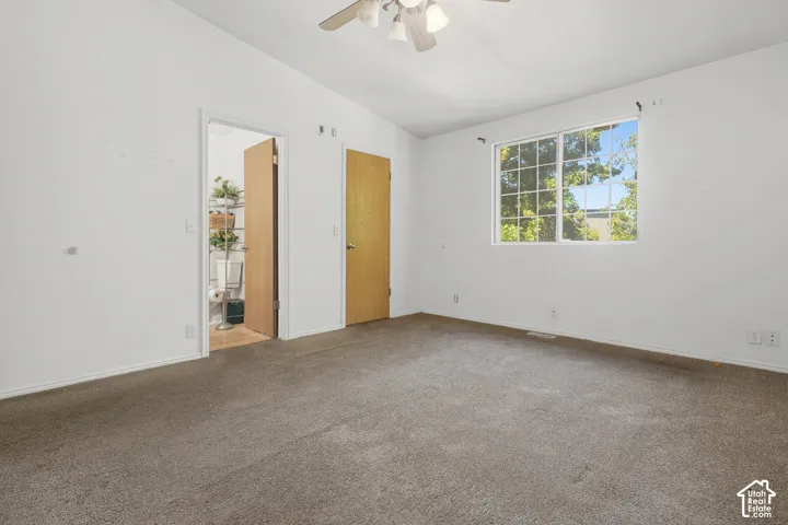 Carpeted flooring, white walls, ceiling fan, window with grid pattern, and wooden doors