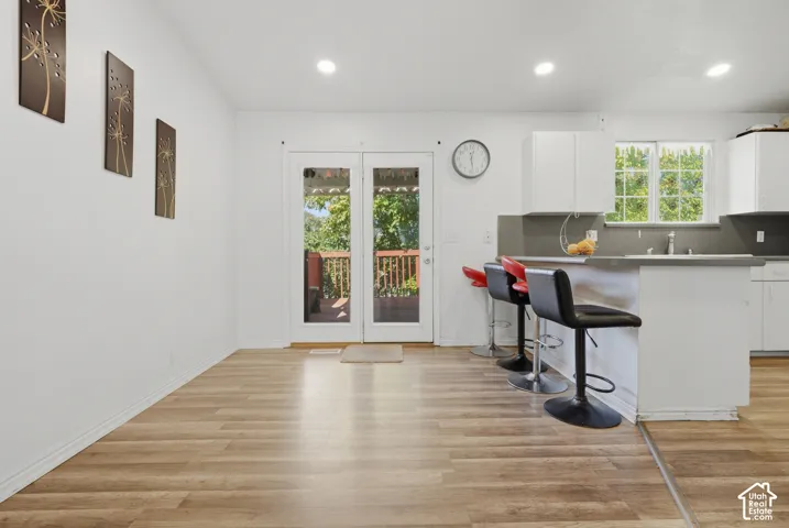 Wood-finish flooring, recessed lighting, white cabinetry, a kitchen island with a breakfast bar, and a glass-paneled door