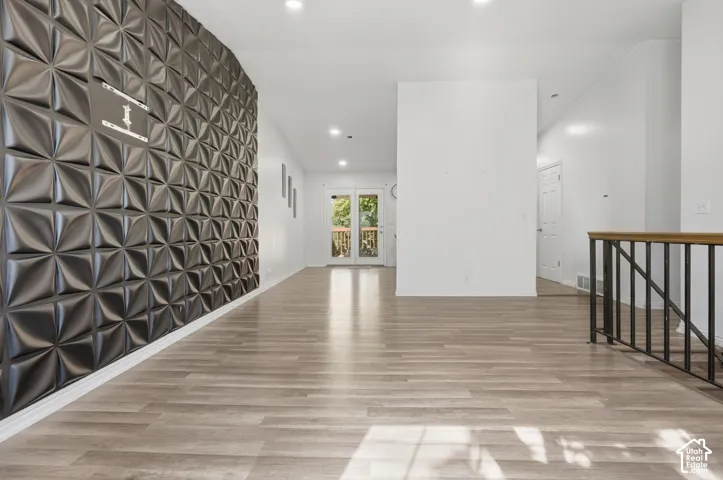 Textured accent wall, wood-finish flooring, recessed lighting, and white walls