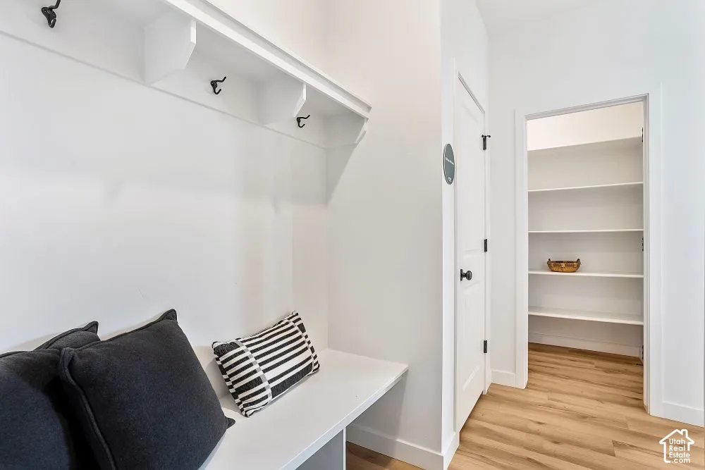 Built-in bench with upper shelving and coat hooks, adjacent to a pantry with multiple shelves