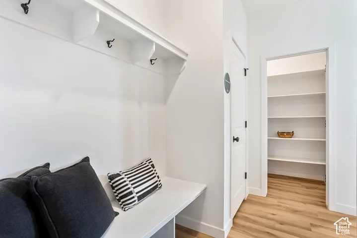 Built-in bench with upper shelving and coat hooks, adjacent to a pantry with multiple shelves