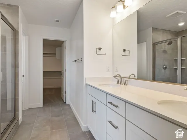Dual vanity with white cabinetry and integrated sinks, brushed nickel fixtures, a large wall-mounted mirror, and a glass-enclosed shower with tiled walls