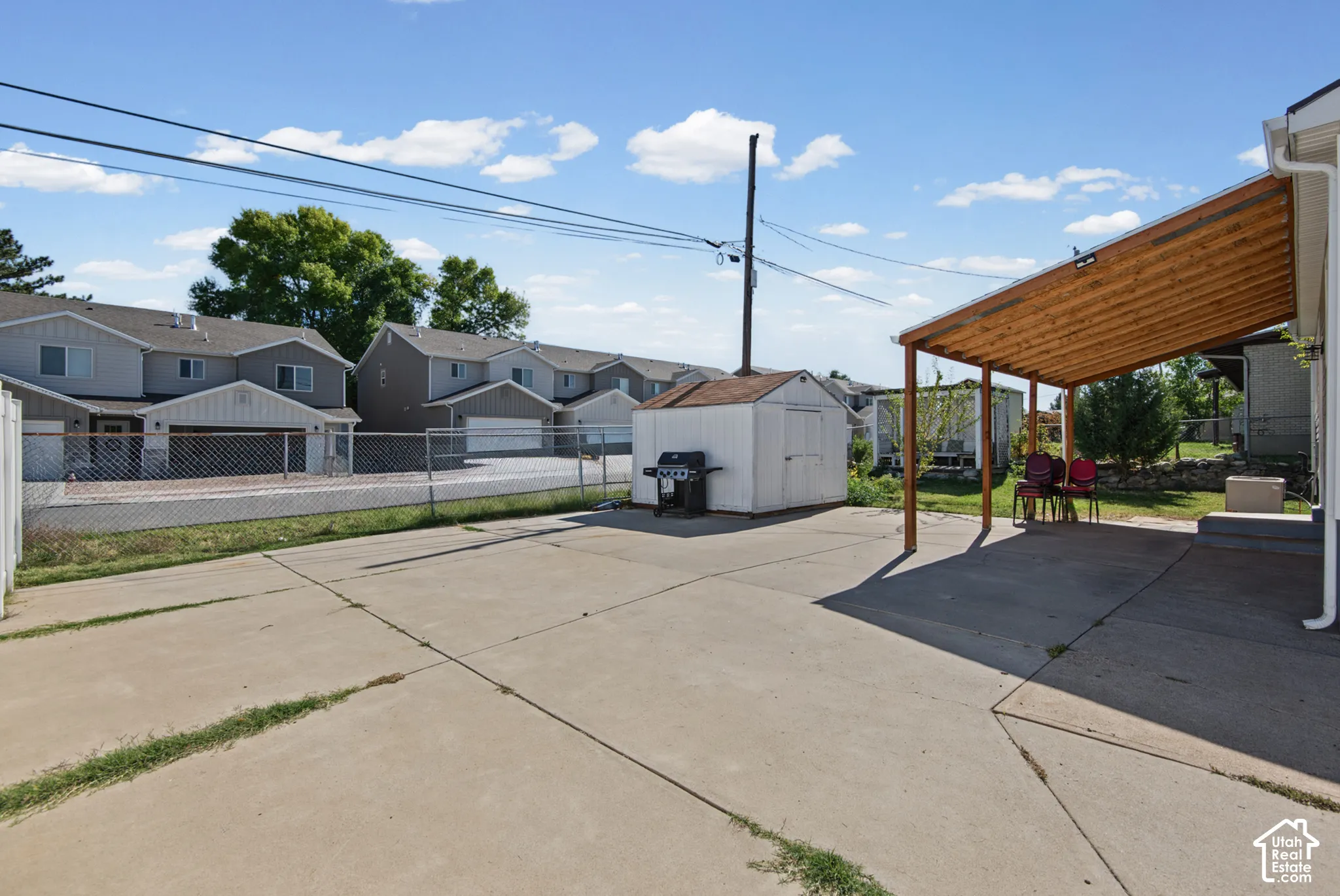 Expansive concrete patio with a wood-beam covered section, featuring an exterior storage shed
