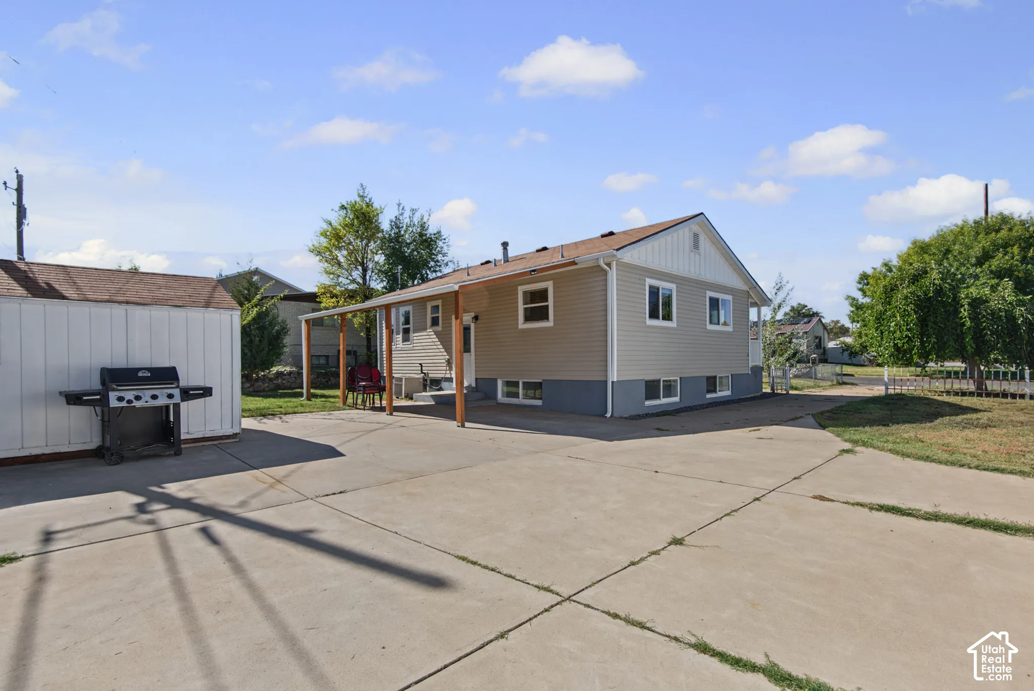 Spacious concrete patio with an attached covered patio, detached storage shed, and mature trees