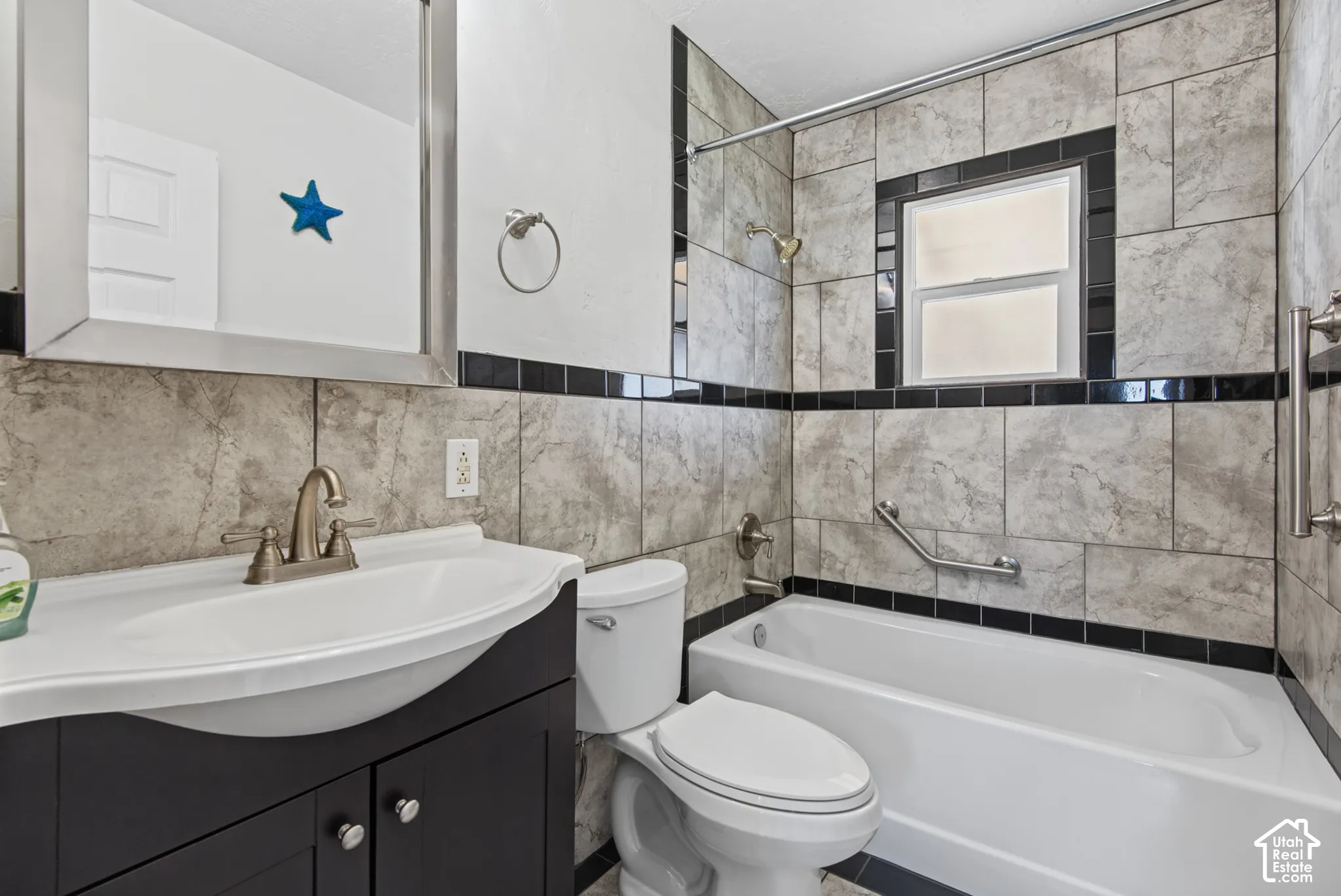 Bathroom featuring full-height tiled walls, a built-in shower over a bathtub, a vanity with a counter-mounted sink, and a mirrored medicine cabinet
